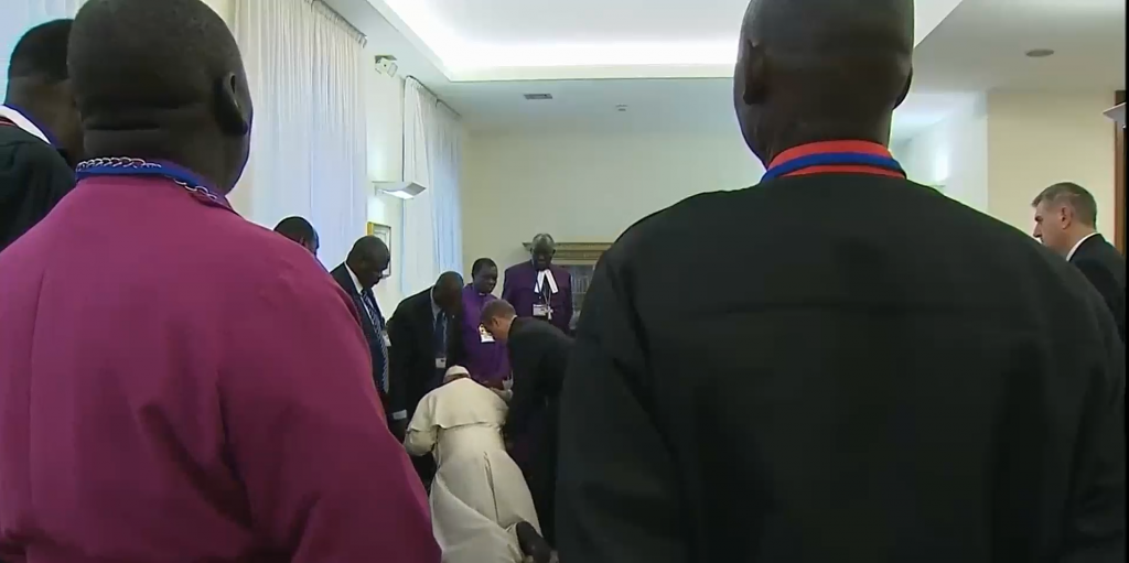 Pope Francis kisses the feet of a Sudanese peace delegate as a crowd looks on.